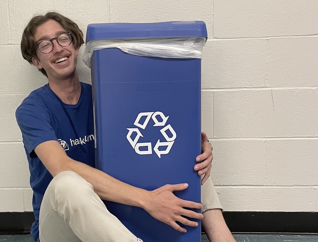 happily hugging a recycle bin with a matching club shirt